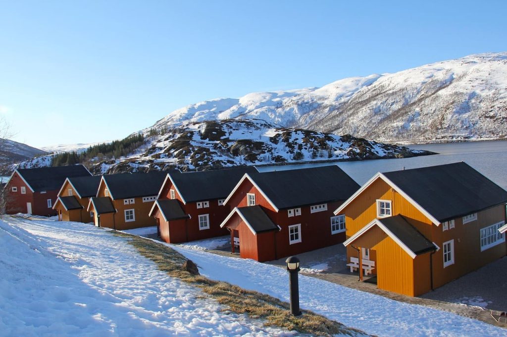Où dormir à Tromsø – rangée de cabanes rouges et jaunes au bord de l’eau avec montagnes enneigées